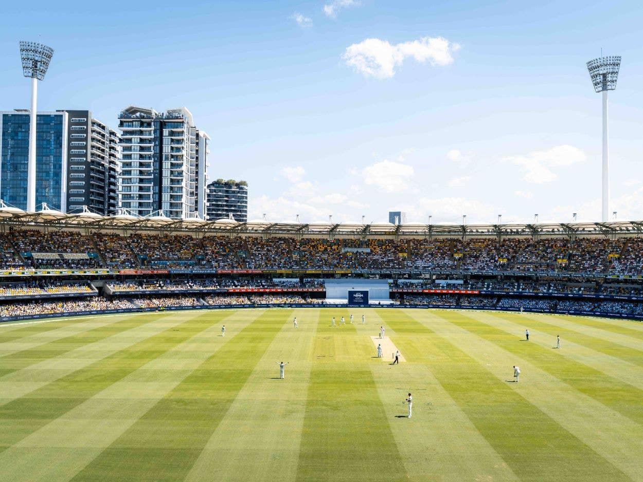View down from the seating bowl onto the field, with players in white clothing on the field during a cricket match