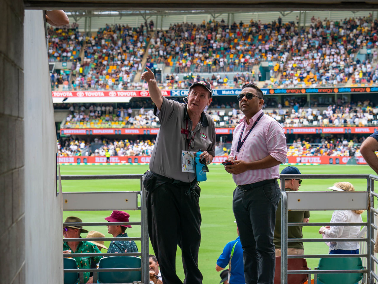 Gabba staff member in Grey polo and black pants, standing beside patron in pink button up shirt, pointing and looking to something in the distance. 